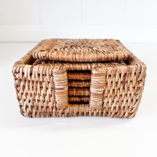 Close-up photo of a square honey brown rattan coaster set with a holder.