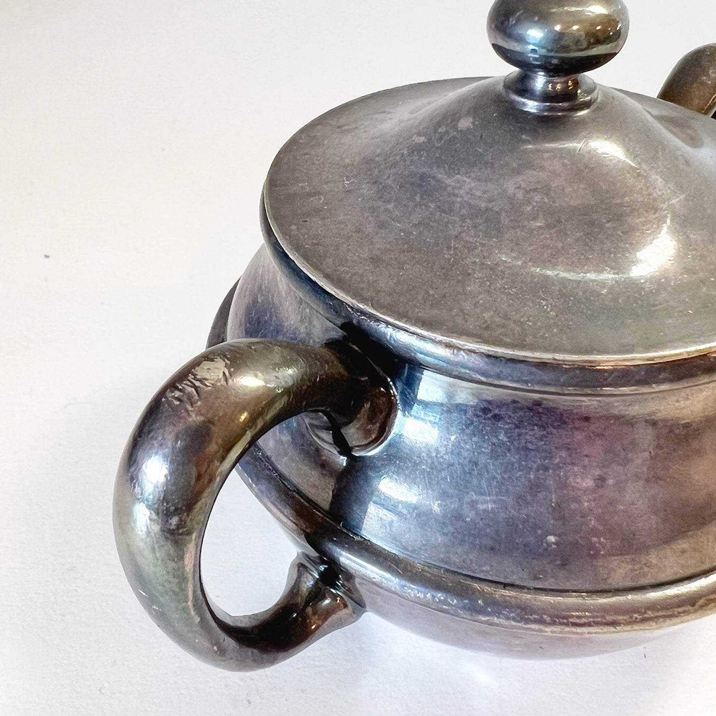 Close-up of a collectible silver sugar bowl with lid, showcasing a high-quality soldered handle seamlessly attached to the body, in a 3/4 top view