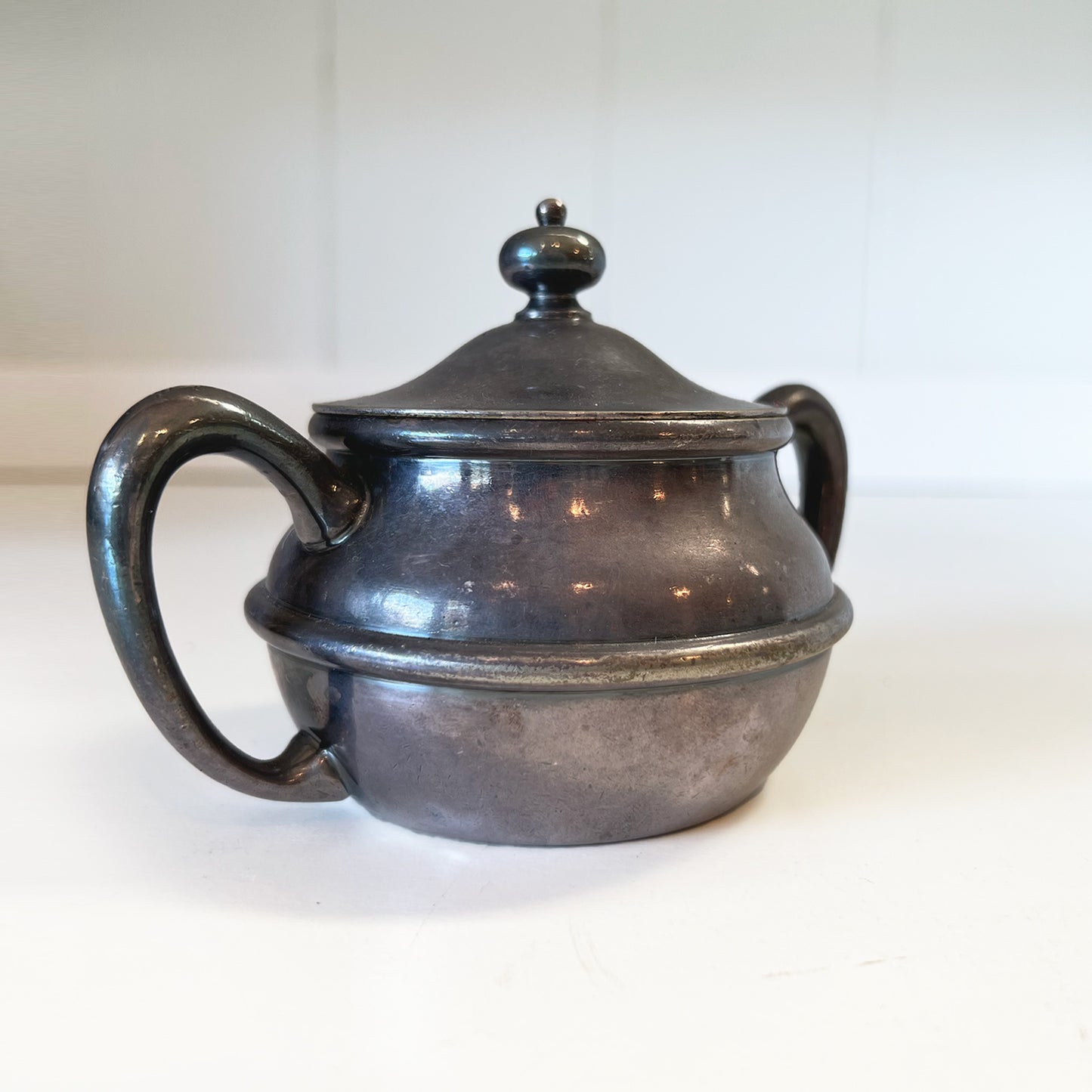 Quaint and tarnished vintage silver sugar bowl with lid, featuring neatly soldered handles, shown in a 3/4 side view