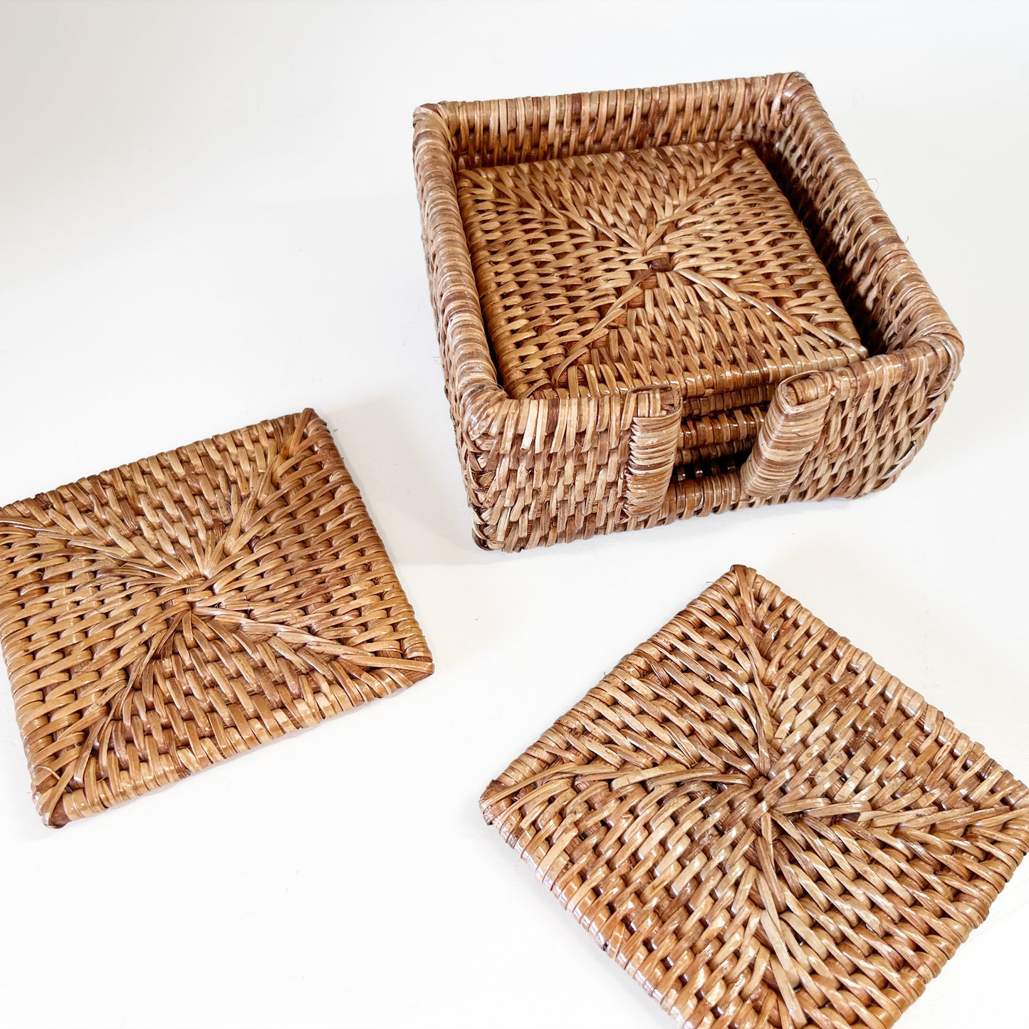 Top view of eco-friendly, handcrafted square rattan coasters in a matching holder