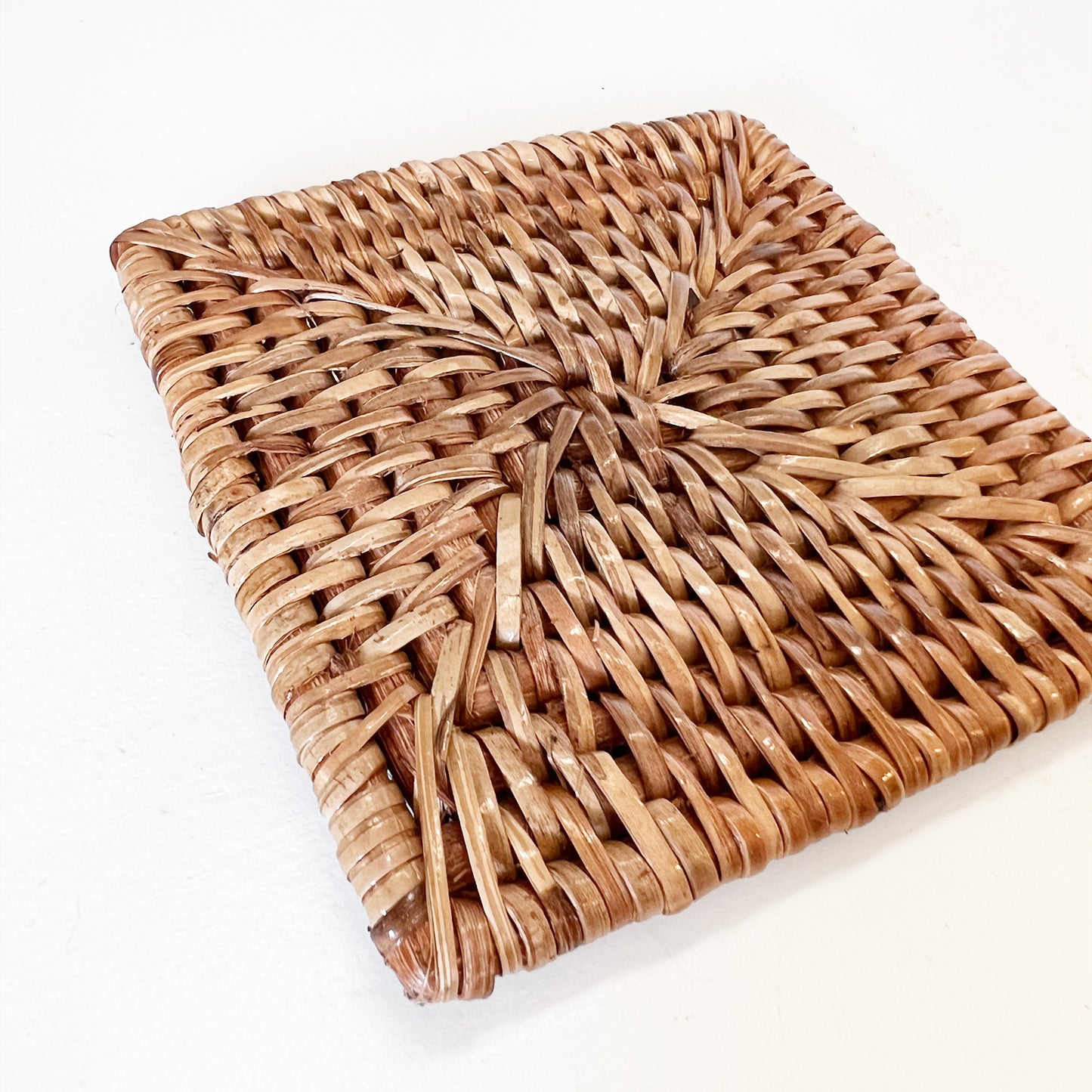 A square rattan coasters with intricate woven patterns.